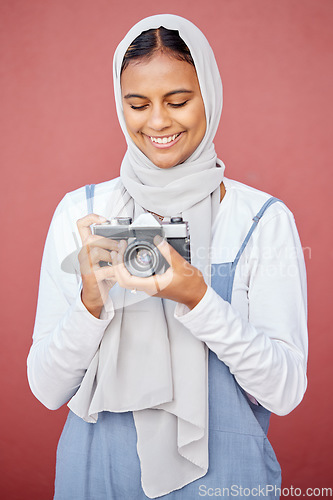 Image of Muslim, hijab and photographer shooting a picture or photo with a retro camera isolated in a studio red background. Islam, Dubai and woman in scarf happy taking creative shots for photography