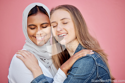 Image of Hug, happy and women friends in a studio with love, care and bond for friendship or support. Happiness, smile and muslim woman embracing a lady from Australia while isolated by a pink background.