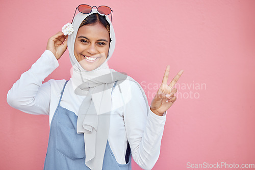 Image of Woman, scarf and flower with peace sign and smile for beautiful casual fashion against pink studio background. Portrait of happy muslim female smiling in happiness and showing hand gesture on mockup