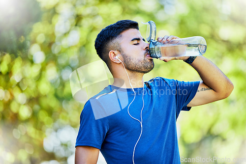 Image of Nature, running and thirst, a man drinking water on fitness break with headphones in park. Health, exercise and freedom, runner in forest with a drink from bottle while on run in natural landscape.