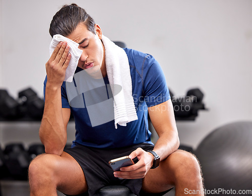 Image of Sweat, tired and man resting in the gym after a intense workout, exercise sports training. Fitness, sport and male athlete networking on social media with a phone after exercising in wellness studio.