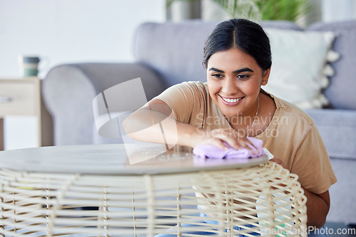Image of Happy, woman and cleaning living room coffee table with household cloth and satisfied smile. Happiness, focus and concentration of young Indian girl polishing lounge furniture in house.