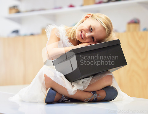 Image of Portrait, children and gift with a girl in a store holding a box while shopping in a mall for retail. Happy, smile and kids with a female child customer hugging a present while sitting on the floor