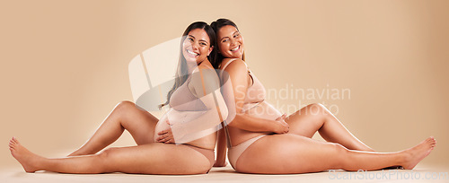 Image of Pregnant woman friends, studio and underwear with smile, sitting and together for support by backdrop. Happy women, pregnancy and solidarity for wellness, care and holding healthy stomach by backdrop