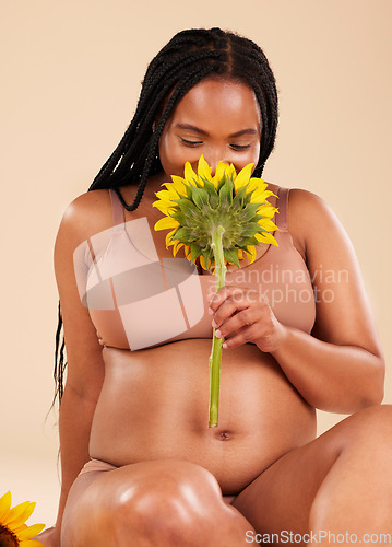Image of Pregnant, maternity and black woman smelling sunflower happy for a baby in her tummy isolated in brown studio background. Young, motherhood and mother smiling for pregnancy holding a plant