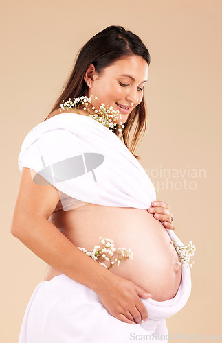 Image of Pregnant, mother and flowers on stomach, healthcare and excited for birth, smile and girl on brown studio background. Pregnancy, woman and mama with tummy, plants and nurture for wellness and growth