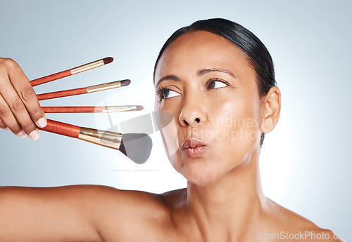 Image of Face, beauty and senior woman with makeup brushes in studio isolated on a gray background. Cosmetics, skincare products and mature female model pout lips with tools to apply foundation and powder.