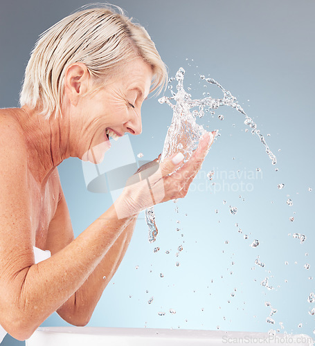 Image of Senior woman, cleaning face and water splash on studio background for beauty, wellness and shower. Happy model, facial skincare drops and washing in bathroom for aesthetic, cosmetics and healthy body
