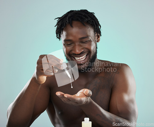 Image of Man, face serum and happy about skincare, beauty and self care product in studio. Healthy black person on blue background for facial oil, dermatology and cosmetics for skin glow, health and wellness