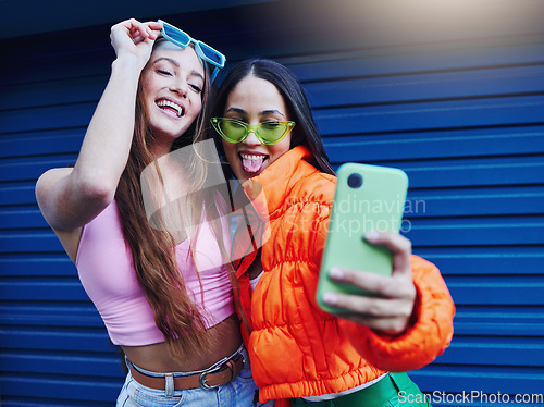 Image of Fashion, selfie and friends with phone on blue background with style, cool sunglasses and urban clothes. Social media, smartphone and women smile for photo on weekend, vacation and holiday in city