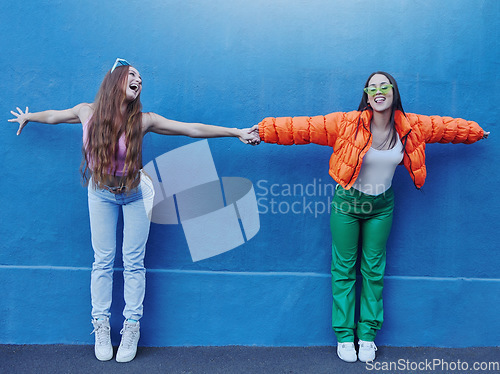 Image of Friends, wall and city for fashion with girl, holding hands and outdoor for funny, comic face or happy together. Gen z women, metro and blue background for trendy clothes, sneakers or urban adventure