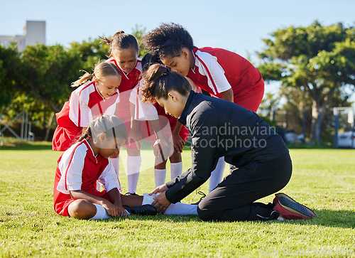 Image of Accident, injury and children soccer team with their coach in a huddle helping a girl athlete. Sports, first aid and kid with a sore, pain or muscle sprain after a match on an outdoor football field.