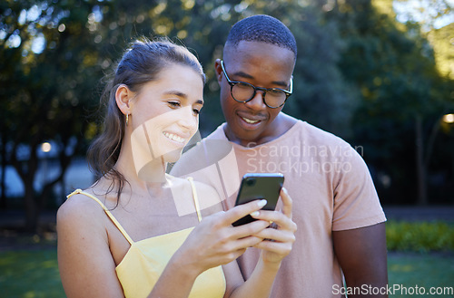 Image of Interracial, meme and couple with a phone in a park, funny communication and laughing at social media. Comic, streaming and black man and woman reading a joke on a mobile in nature of France