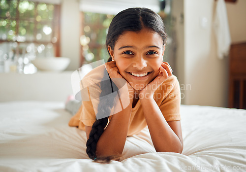 Image of Portrait, children and bedroom with an indian girl lying on her bed at home over the weekend to relax. Kids, face and smile with a happy female child resting or relaxing alone in her house
