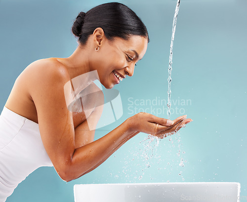 Image of Black woman, cleaning and water splash on blue background for skincare, wellness and beauty. Happy model, facial shower drops and washing basin in bathroom studio for aesthetic, cosmetics and smile