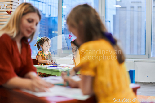 Image of Creative kids during an art class in a daycare center or elementary school classroom drawing with female teacher.