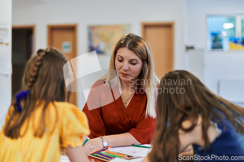 Image of Creative kids during an art class in a daycare center or elementary school classroom drawing with female teacher.