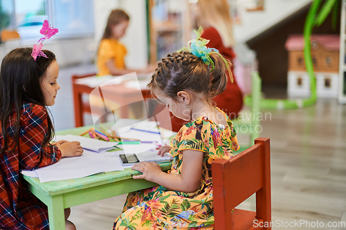 Image of Creative kids during an art class in a daycare center or elementary school classroom drawing with female teacher.