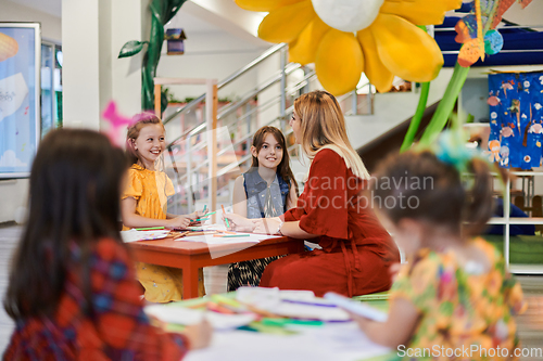 Image of Creative kids during an art class in a daycare center or elementary school classroom drawing with female teacher.