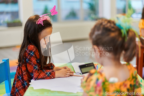 Image of Creative kids during an art class in a daycare center or elementary school classroom drawing with female teacher.