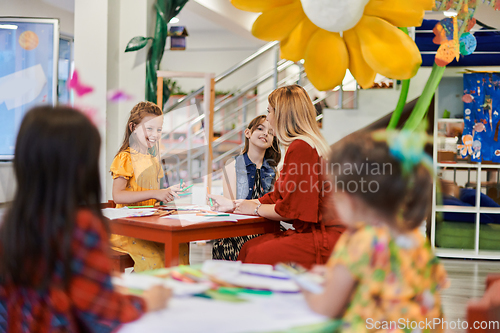 Image of Creative kids during an art class in a daycare center or elementary school classroom drawing with female teacher.