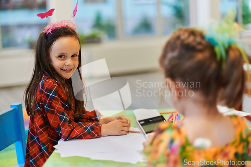 Image of Creative kids during an art class in a daycare center or elementary school classroom drawing with female teacher.