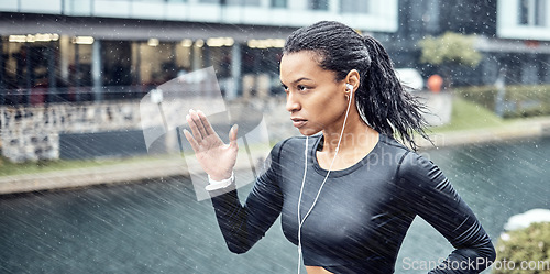 Image of Black woman, fitness and running with earphones in the rain for sports motivation or determination in the city. African American sporty female runner doing intense cardio workout in the rainy weather