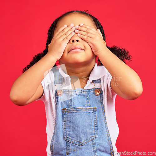 Image of Little girl, hands and eyes cover on isolated red background for shy, mistake expression and peekaboo games. Child, kid and youth in hide and seek activity, surprise gesture or blind emoji on studio