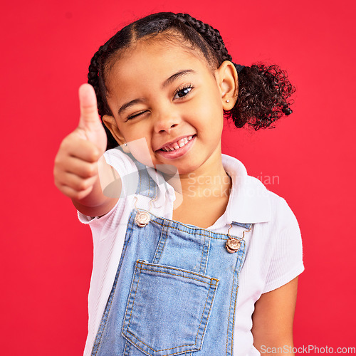 Image of Thumbs up, portrait and girl child in studio, red background or isolated hand sign. Happy kids, thumb gesture and wink face of like emoji, support and vote of trust, thanks or yes agreement of review