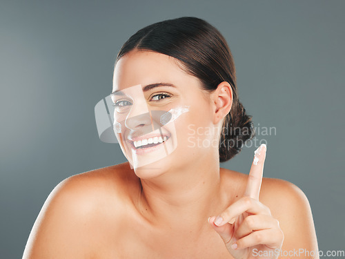 Image of Portrait, skincare and woman with cream, cosmetics and smile with girl on grey studio background. Face, female and happy lady with lotion, creme and dermatology for treatment and grooming routine