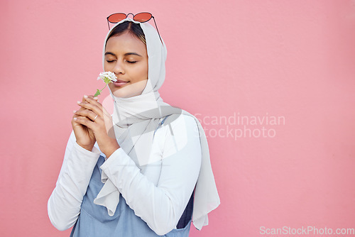 Image of Young Islamic girl, smell flower and modern gen z or millennial fashion, zen freedom and calm peace in pink background. Muslim female, flowers scent and hijab with trendy or edgy clothes in studio