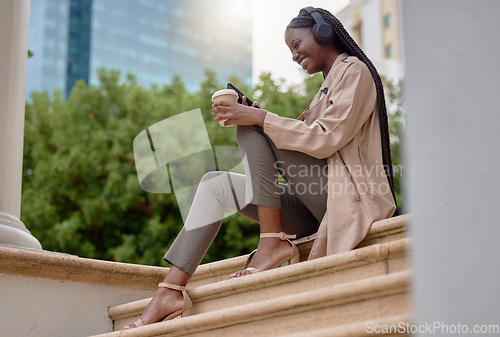 Image of Music headphones, phone and black woman with coffee while sitting on city steps. Technology, tea break and happy female employee with caffeine and mobile for social media, streaming radio or podcast.