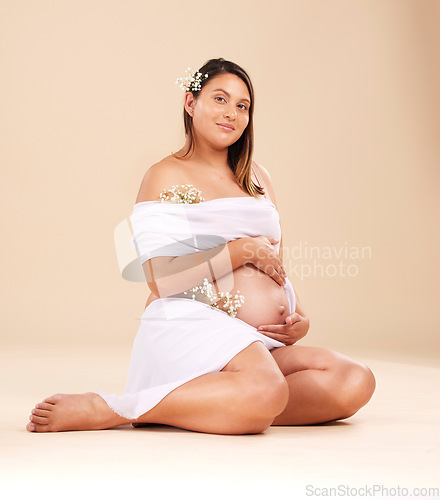 Image of Pregnancy, beauty and portrait of a woman in studio with chiffon material and flowers holding her stomach. Maternity, prenatal health and pregnant female model with floral posing by beige background.