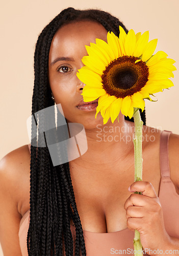 Image of Portrait, beauty and sunflower with a black woman in studio on a beige background for natural treatment or body positivity. Spring, flower and skincare with a young female posing for wellness