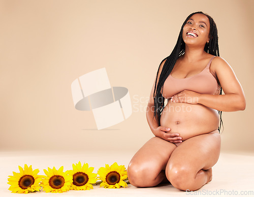 Image of Pregnancy, mother and portrait of pregnant black woman with sunflower plants happy isolated in brown studio background. Baby, motherhood and future mom holding her tummy, stomach or abdomen for care