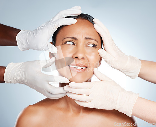 Image of Plastic surgery, scared and face of woman with hands from doctors isolated on blue background. Skincare, check and senior person worried about botox, cosmetic and facial surgery with professionals