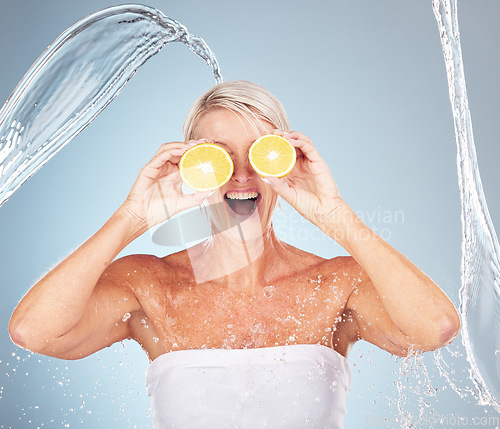 Image of Water splash, studio and woman with lemon for wellness, healthcare or vitamin c by blue background. Happy senior model, citrus fruit and cosmetic skincare for happiness, excited or water drop on skin