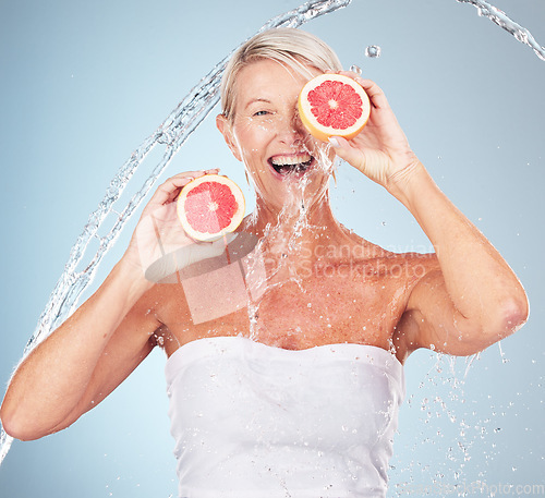 Image of Woman, studio portrait and grapefruit with water splash, smile and happy for wellness by blue background. Senior model, organic citrus fruit and vitamin c for health, nutrition and self care process