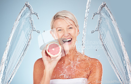 Image of Woman, grapefruit and studio portrait with water splash, happiness and cosmetics for wellness by blue background. Senior model, citrus fruit and vitamin c for health, nutrition and self care process