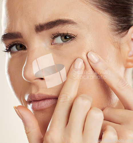 Image of Portrait, hands and pimple with a woman checking or examining her skin for acne problems in studio. Face, fingers and breakout with an attractive young female indoor to squeeze or pop a blackhead