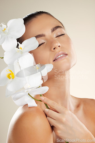 Image of Skincare, beauty and woman with orchid flower on skin for natural dermatology cosmetic product. Glow on face of aesthetic model in studio for sustainable floral plant for makeup and spa wellness