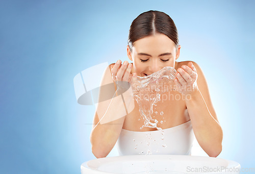 Image of Woman, beauty and water splash for clean face or skin with natural dermatology cosmetic product. Happy aesthetic model in studio for health and wellness or self care spa facial on blue background