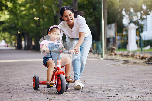 Image of Mother, kid and bicycle teaching with training wheels for learning, practice or safety at the park. Happy mom helping little girl to ride a bike with smile for proud playful moments in the outdoors
