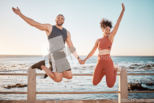 Image of Fitness, energy and portrait of a couple jumping at beach for training fun, support and celebration of goal. Jump, happy and excited man and woman holding hands at the sea for cardio in Spain