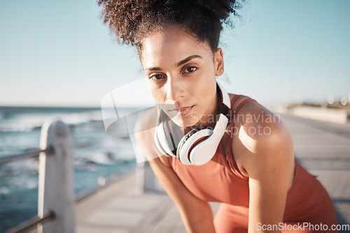 Image of Portrait, fitness and black woman tired, ocean and runner with headphones, focus and determined for goal. African American lady, female exhausted and athlete with podcast, rest or training for health