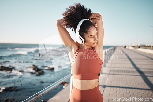 Image of Beach, headphones and woman stretching for a fitness exercise, running or training for a race or marathon. Health, sports and female athlete doing an arm warm up before a cardio workout by the ocean.