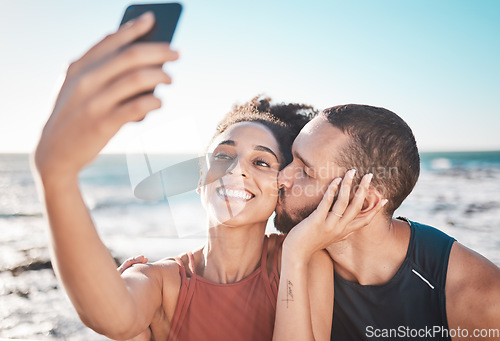 Image of Selfie kiss, love and couple with a phone for streaming, training and care at the beach in Bali. Gratitude, exercise and affectionate man and woman with a smile for a mobile photo after a workout