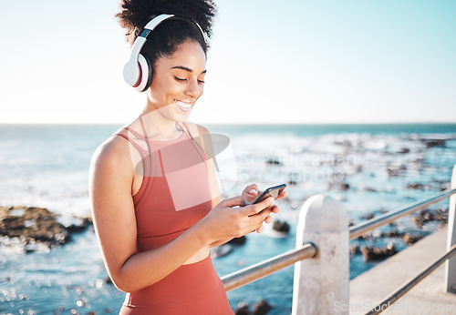 Image of Black woman at beach, headphone and phone with fitness, runner listening to music for sports motivation. Happy, streaming online with podcast or radio, smartphone and running by sea with calm outdoor