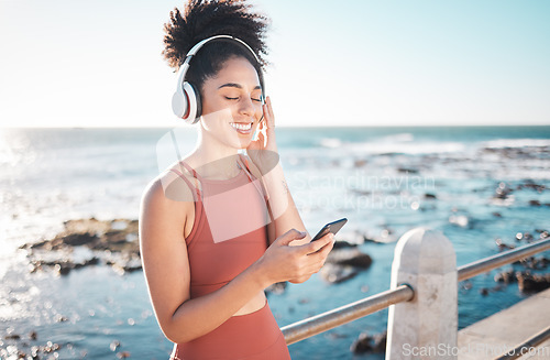 Image of Black woman at beach, headphone and smartphone with fitness, runner listening to music for sports motivation. Happy, streaming online with podcast or radio, phone and running by sea with calm outdoor