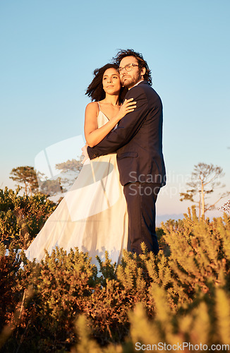 Image of Interracial couple, love and wedding at sunset, hug and happy for romance and relationship in nature. Marriage, bride and groom hug at outdoor ceremony and sweet on blue sky background space